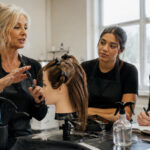 Beauty instructor teaching students with a mannequin head and salon tools in a classroom training setting