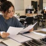 Future cosmetology student compares blank state requirement papers, hour tracker, combs, clips, and mannequin head before enrolling in beauty school.